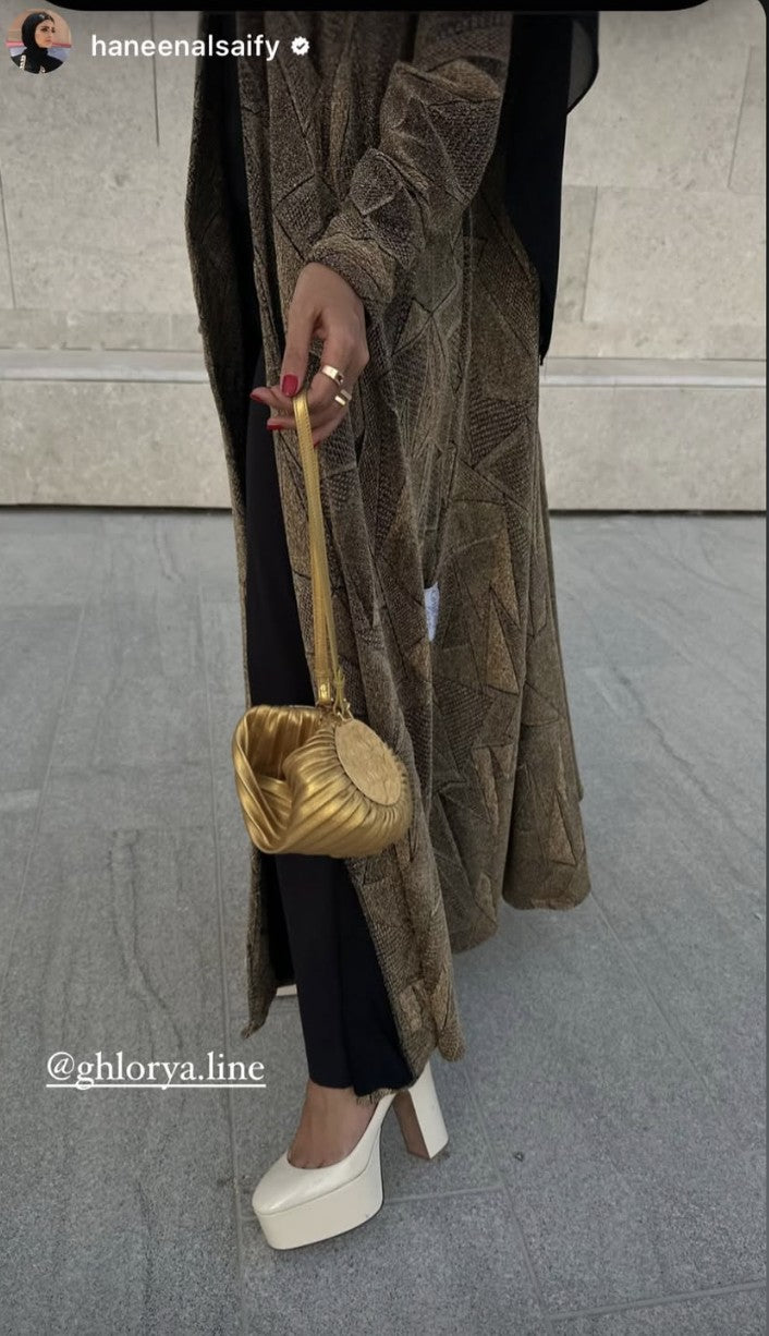 Detail of a geometric Ghlorya abaya styled with a gold handbag